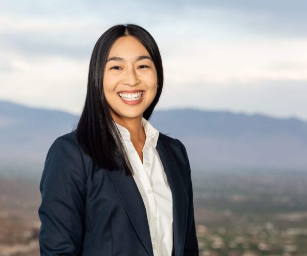 A Smiling Woman Standing In Front Of A Mountain