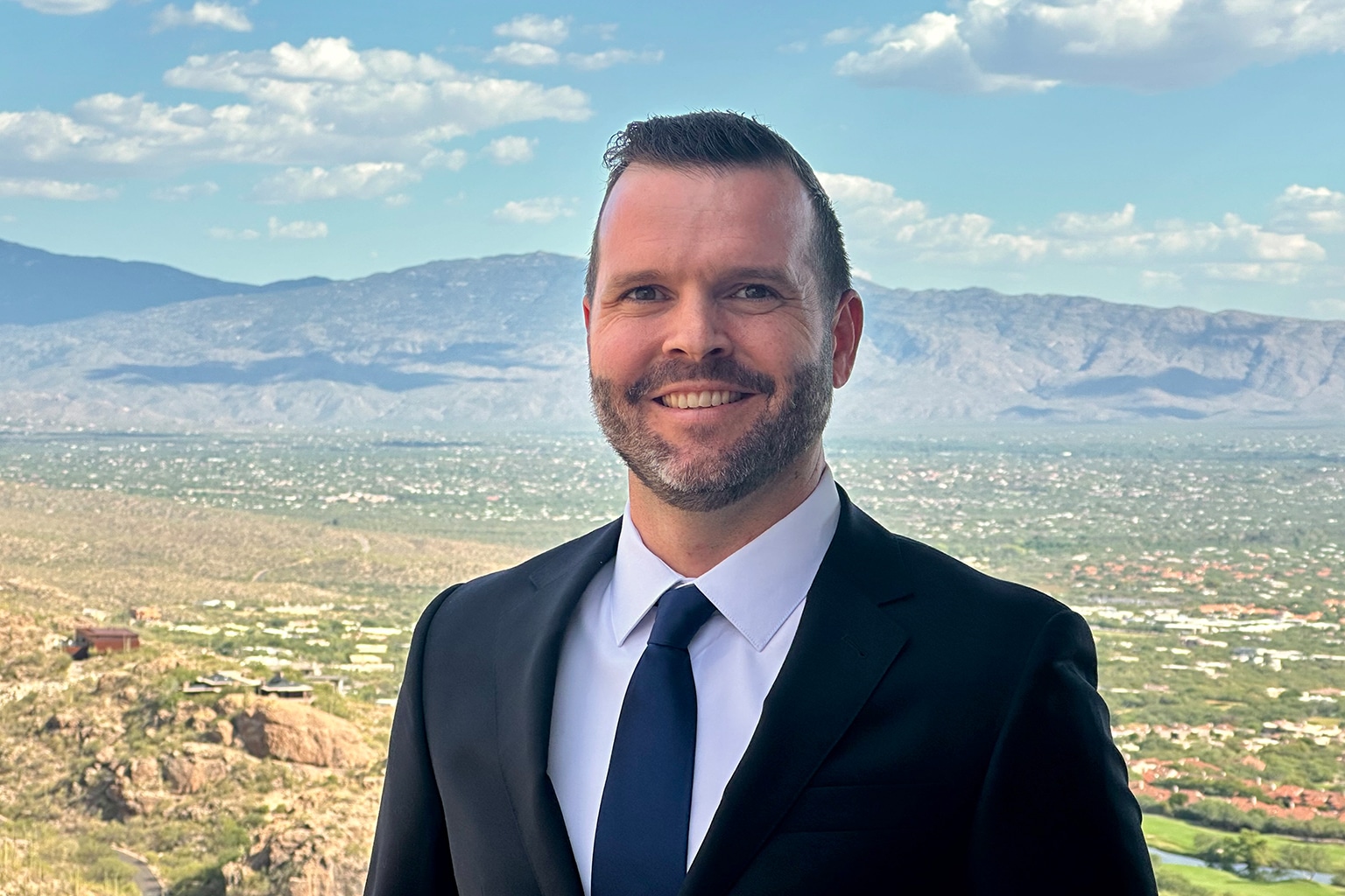 a man wearing a suit and tie standing in front of a mountain